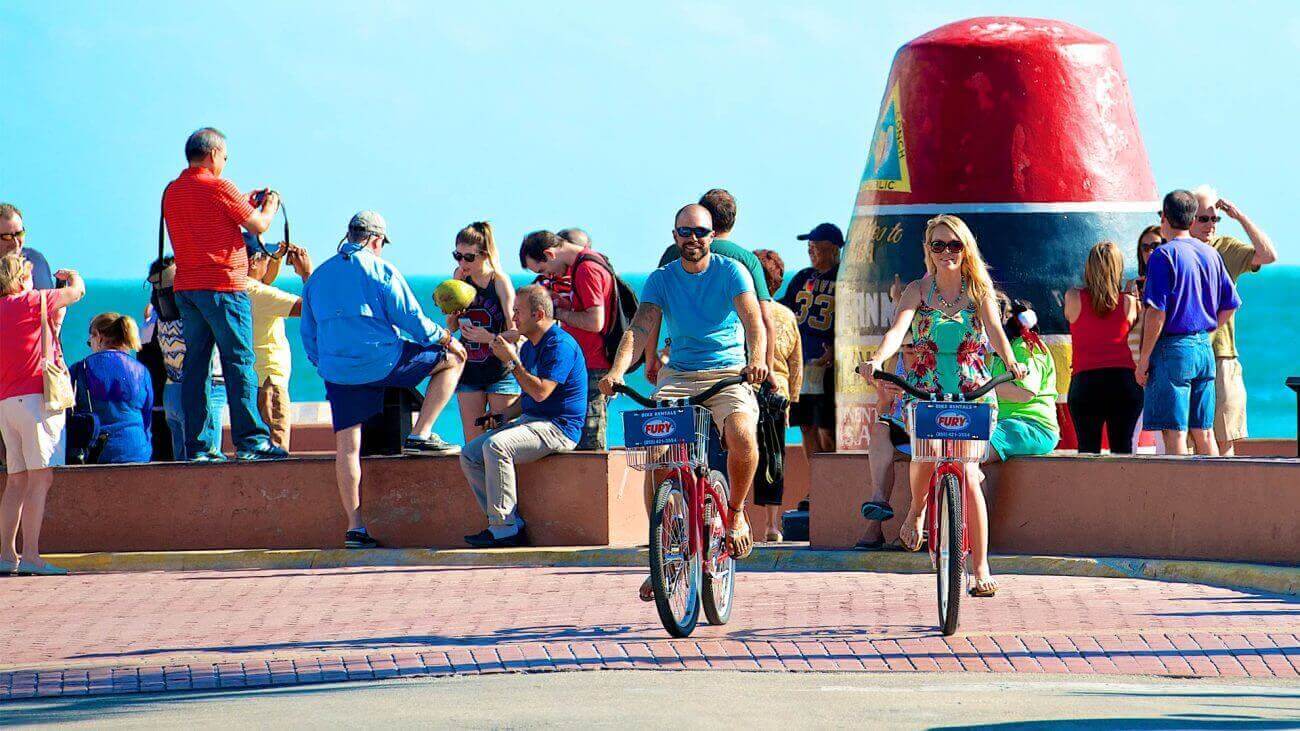A couple riding bikes, at the Southernmost point, in Key West, Florida
